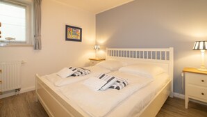 Ein Schlafzimmer mit einem Bett, zwei Nachttischen, einem Fenster mit Vorhängen, einer Heizung und einem Wandbild.
