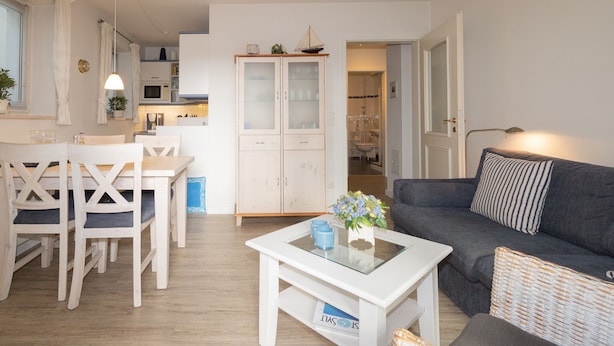 Ein modernes Wohnzimmer mit einem weißen Couchtisch, einer grauen Couch und einem Essbereich mit weißen Stühlen.