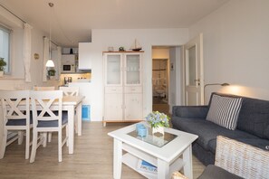 A modern living room with a white coffee table, grey sofa, and a dining area with white chairs. - Very lovingly and personally furnished apartment. (Hörnum auf Sylt)