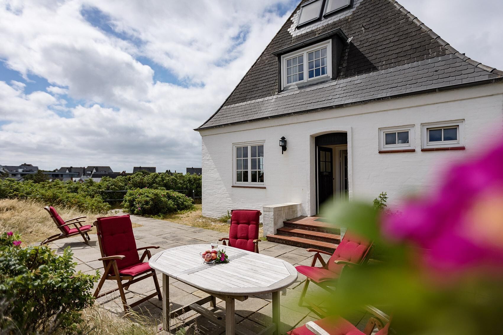 A white house with a grey roof, a small porch, and a table with chairs.