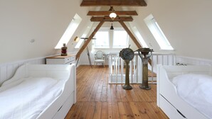 Ein Schlafzimmer im Loft-Stil mit zwei weißen Betten, Holzbalken, geneigten Decken und Dachfenstern.
