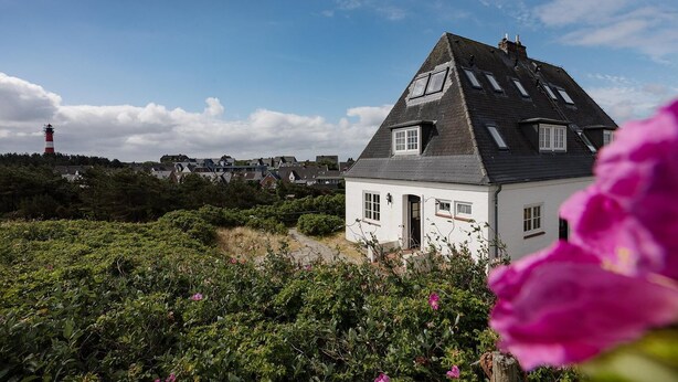 Ein weißes Haus mit einem steilen Satteldach, einer kleinen Veranda und einem sichtbaren Schornstein.