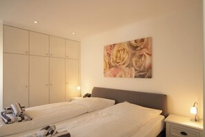 Une chambre d’hôtel avec deux lits, une armoire, une table de chevet avec une lampe et un tableau floral accroché au mur.