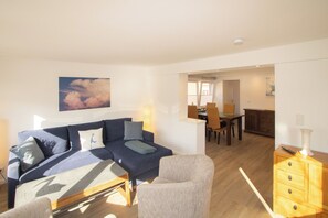 Un salon comprenant un canapé, des fauteuils, un meuble en bois et un coin repas avec des chaises et une table.