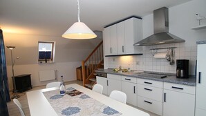 Une cuisine moderne avec des armoires blanches, une hotte de cuisinière en acier inoxydable et un comptoir en granit. On y trouve une table à manger avec un chemin de table à motifs floraux et des chaises.
