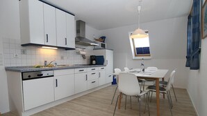 Une cuisine moderne avec des meubles blancs, une table à manger avec des chaises et une fenêtre laissant entrer la lumière naturelle.