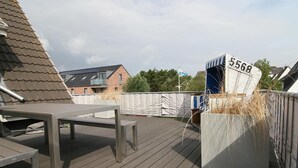 Um deck de madeira com um banco e um jardim com gramíneas altas.
