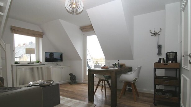 Um apartamento estilo loft com área de jantar, televisão e cozinha compacta.