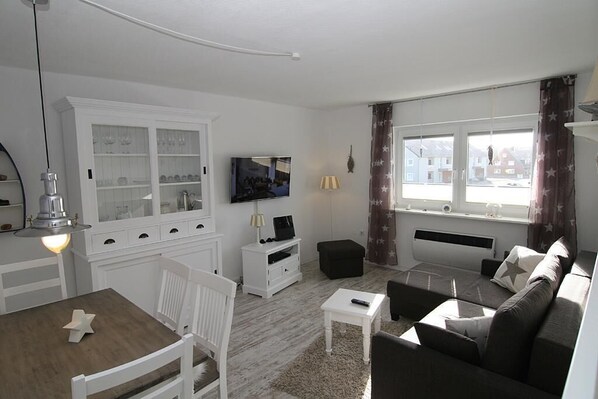 A living room with a white cabinet, a TV, a sofa, and a dining table. - Wonderful vacation apartment, suitable for 4 people (Hörnum auf Sylt)