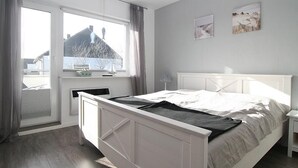 A bedroom with a bed, a window, a bedside table, and a wall with two pictures. - Wonderful vacation apartment, suitable for 4 people (Hörnum auf Sylt)