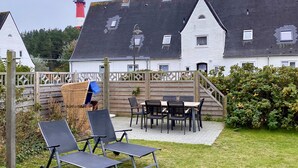 Een terras met buitenmeubilair, een houten omheining en uitzicht op een wit gebouw met een rood-wit gestreepte vuurtoren op de achtergrond.
