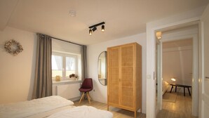 Een slaapkamer met twee bedden, een kledingkast, een spiegel, een stoel en een raam met gordijnen.