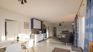 A modern kitchen with white cabinets, a dining area with a table and chairs, and a living area with a sofa and a TV. - This 3-room vacation apartment is spacious and on the ground floor (Hörnum auf Sylt)