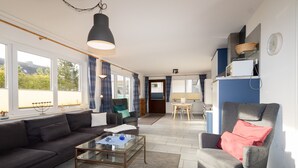 A living room with a sofa, armchair, coffee table, and a dining area with a table and chairs. - This 3-room vacation apartment is spacious and on the ground floor (Hörnum auf Sylt)