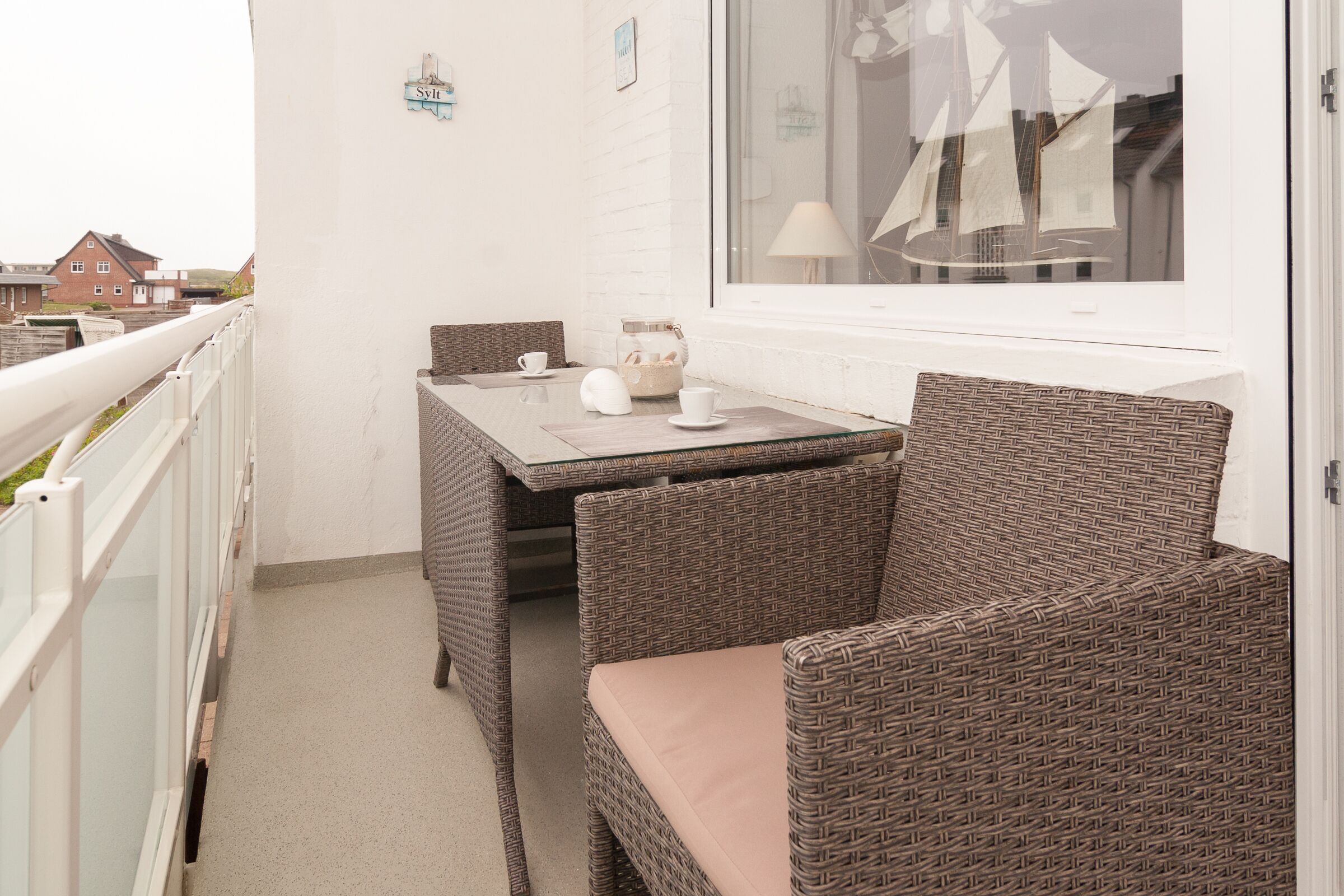 A balcony with wicker furniture, a table, and a window with a view of sailboats.