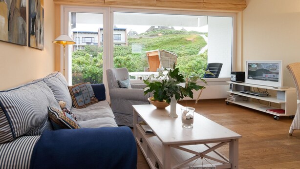 A modern living room with a sofa, armchair, coffee table, and a TV. - Vacation apartment for up to 4 people (2 adults + 2 children) (Hörnum auf Sylt)