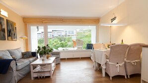 A modern living room with a sofa, a coffee table, and wicker chairs around a dining table. - Vacation apartment for up to 4 people (2 adults + 2 children) (Hörnum auf Sylt)