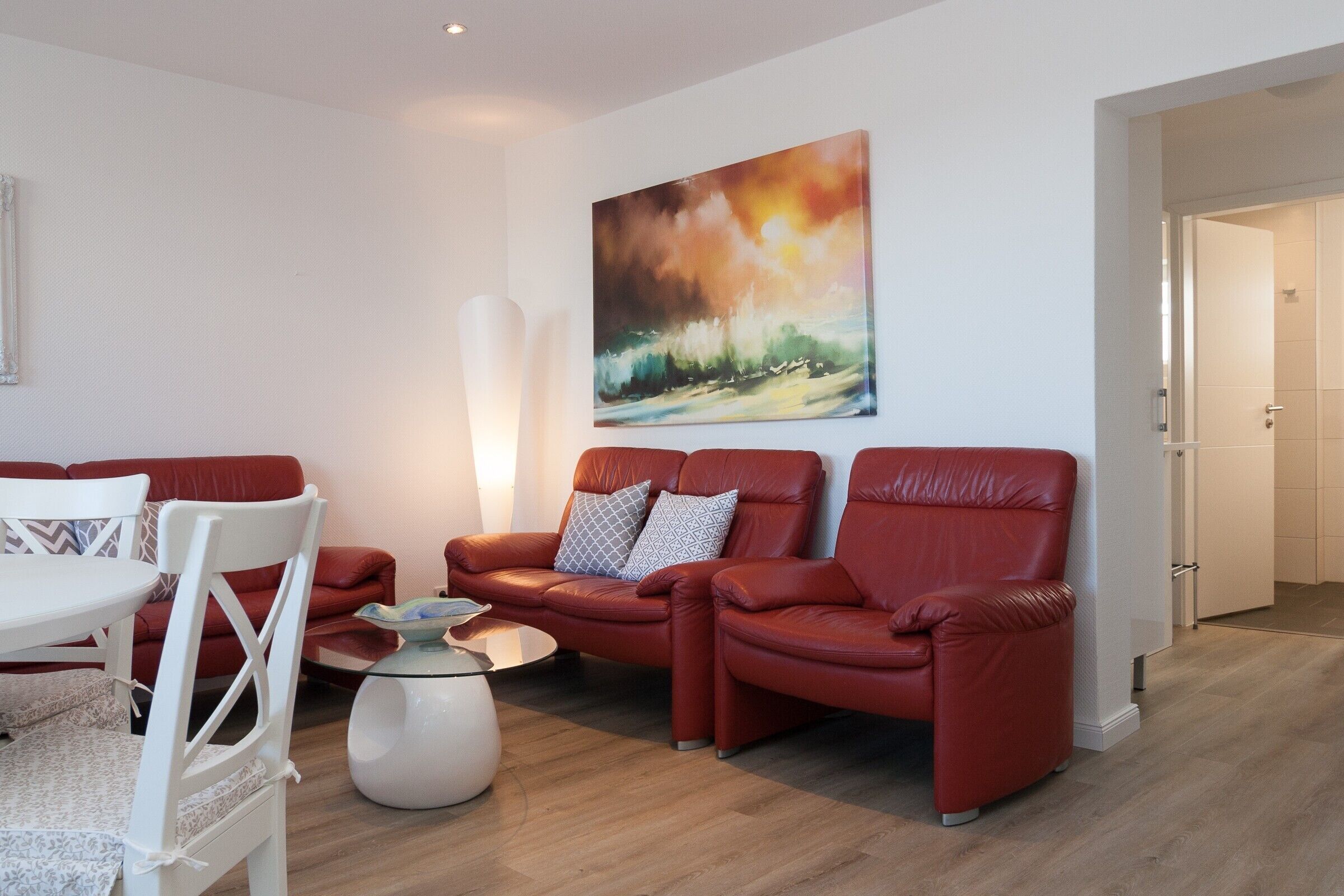 A modern living room with a red leather sofa, a white coffee table, and a painting on the wall.