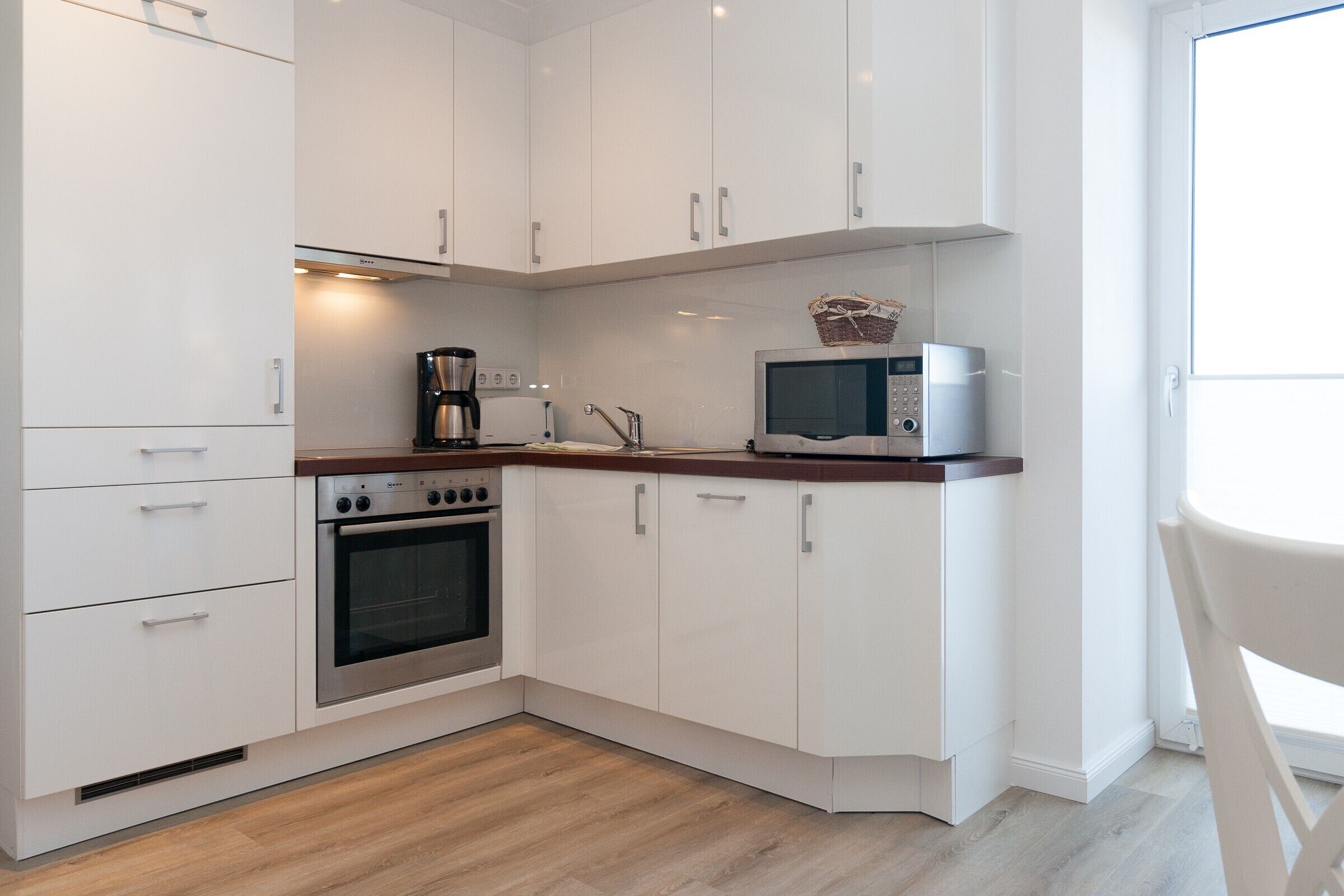 Een moderne keuken met witte kasten, een roestvrijstalen oven, een magnetron en een koffiezetapparaat.