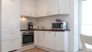 A modern kitchen with white cabinets, a stainless steel oven, a microwave, and a coffee maker. - Directly on the beach with a view of the sea (Hörnum auf Sylt)