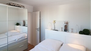 A modern bedroom with two beds, a large mirror, and a bedside table with decorative items. - Directly on the beach with a view of the sea (Hörnum auf Sylt)