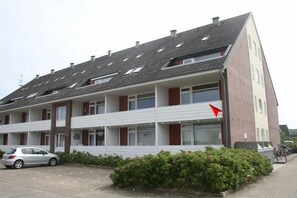 Een meerlaags woongebouw met een schuin dak, balkons en een parkeerplaats met een auto.