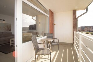 A balcony with wicker furniture, a small table, and a view of the neighborhood.