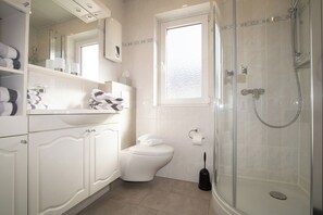 Een moderne badkamer met een douchecabine van glas, een toilet en een wastafel met spiegel erboven.