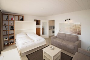 Een slaapkamer met een bed, een bank, een salontafel, een boekenkast en een keukenhoek.