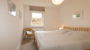 Une chambre à coucher avec un lit, une fenêtre, une chaise et des tableaux encadrés accrochés au mur.