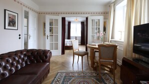 Ein Wohnzimmer mit braunem Ledersofa, einem Holzesstisch mit zwei Stühlen, einem Fernseher und einem gemusterten Teppich.