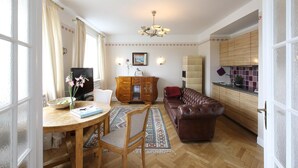 Ein Wohnzimmer mit Esstisch aus Holz, einer Ledersofa, einem Fernseher und einem gemusterten Teppich.
