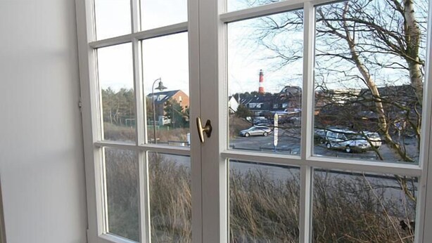 Ein Zimmer mit großem Fenster, das auf einen Parkplatz und ein Gebäude mit einem rot-weiß gestreiften Turm blickt.