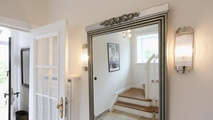 A hallway with a large mirror, a door with frosted glass panels, and a staircase with a light fixture above it.
