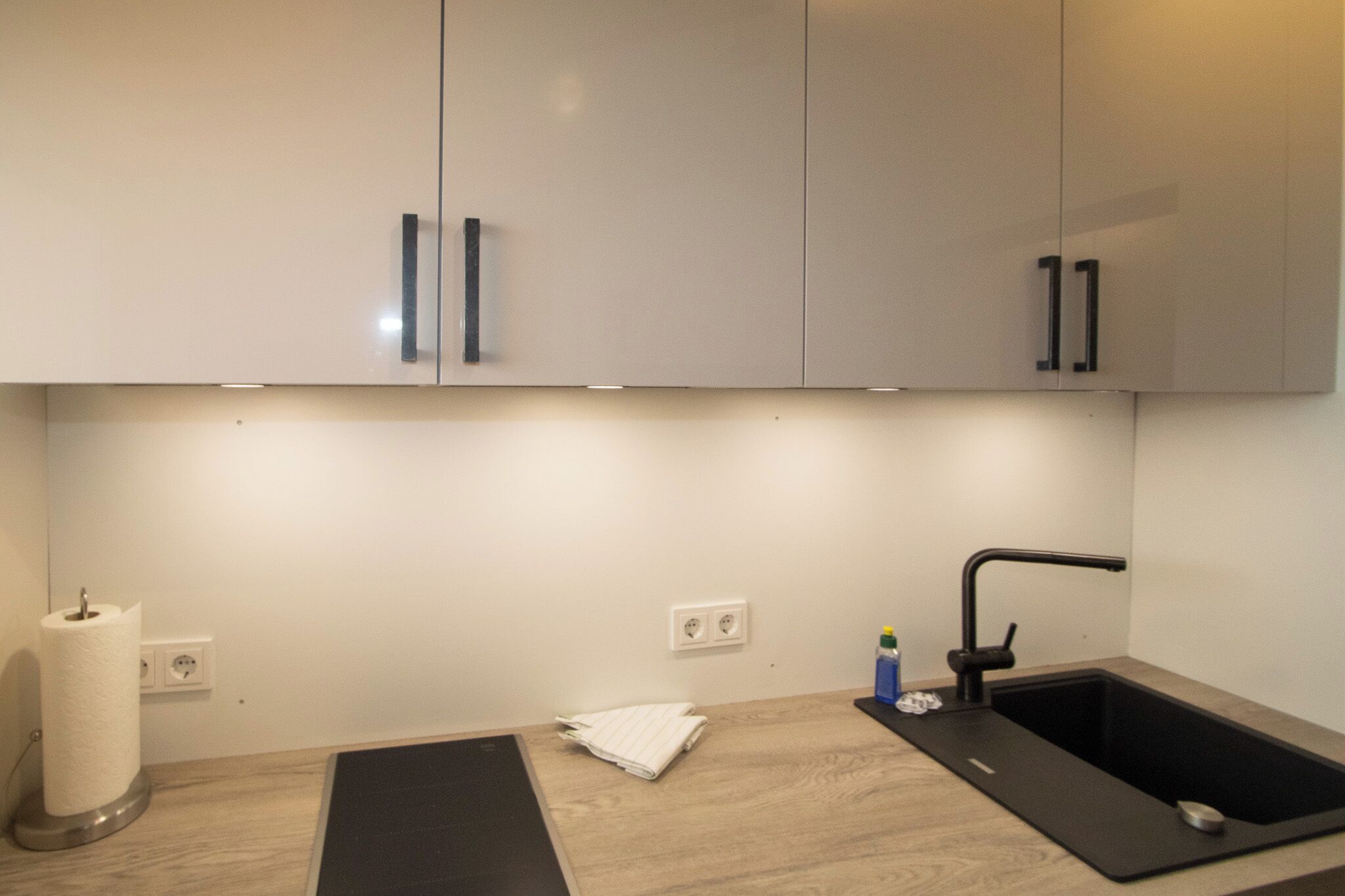 Une cuisine moderne avec des meubles blancs, un plan de travail noir et un évier noir.