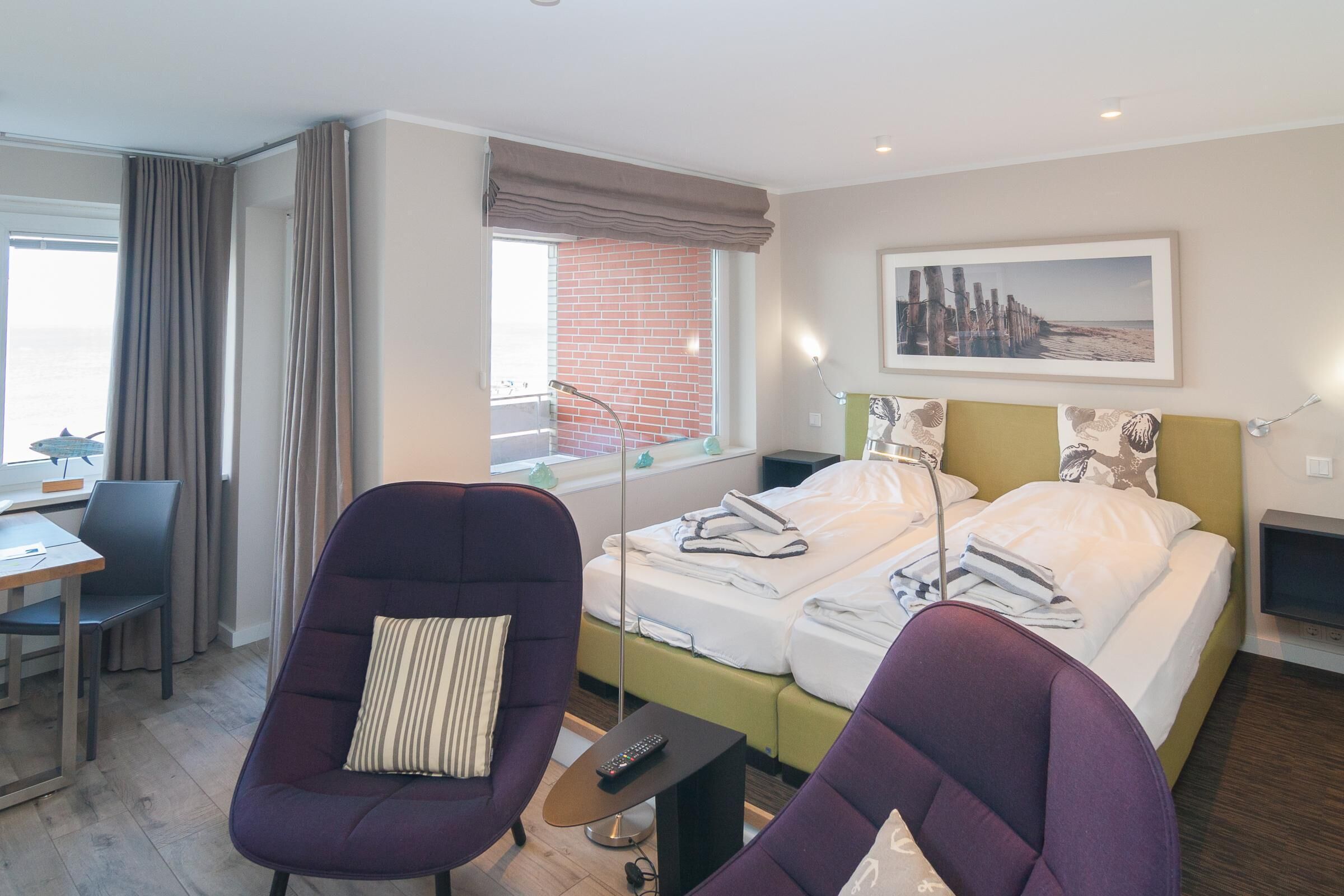Ein Hotelzimmer mit Bett, zwei Stühlen, einem Schreibtisch und einem fensterbepflanzten Fenster.