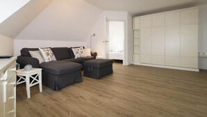 Ein Schlafzimmer im Loft-Stil mit schrägverdeckter Decke, einer dunkelgrauen Sofagarnitur, einem weißen Kleiderschrank und einem kleinen weißen Beistelltisch.