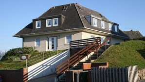Ein zweistöckiges Haus mit steiler Satteldach, einer Holztreppe und einer Ziegelwand.