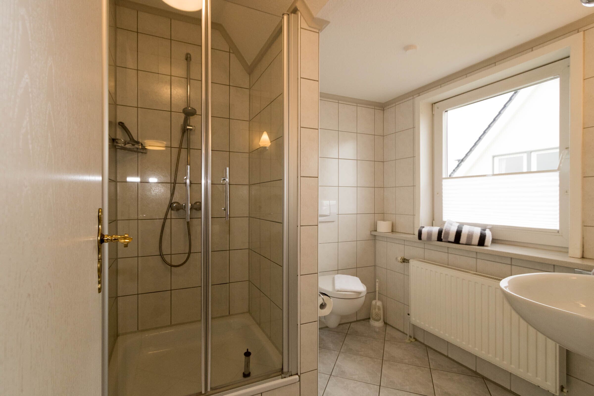 Une salle de bain avec une douche à parois de verre, des toilettes et un lavabo, avec une fenêtre au-dessus.