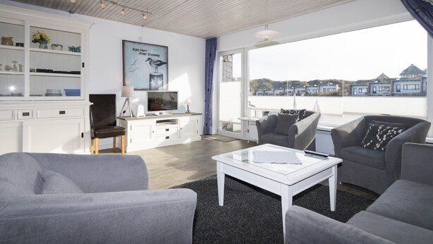 A modern living room with a large window, a flat-screen TV, and a cozy seating area. - Cozy vacation apartment in the immediate vicinity of.... (Hörnum auf Sylt)