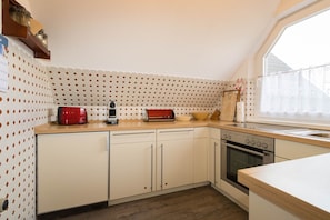 Une cuisine avec des meubles blancs, un grille-pain rouge, une cuisinière et une fenêtre donnant sur un beau paysage.