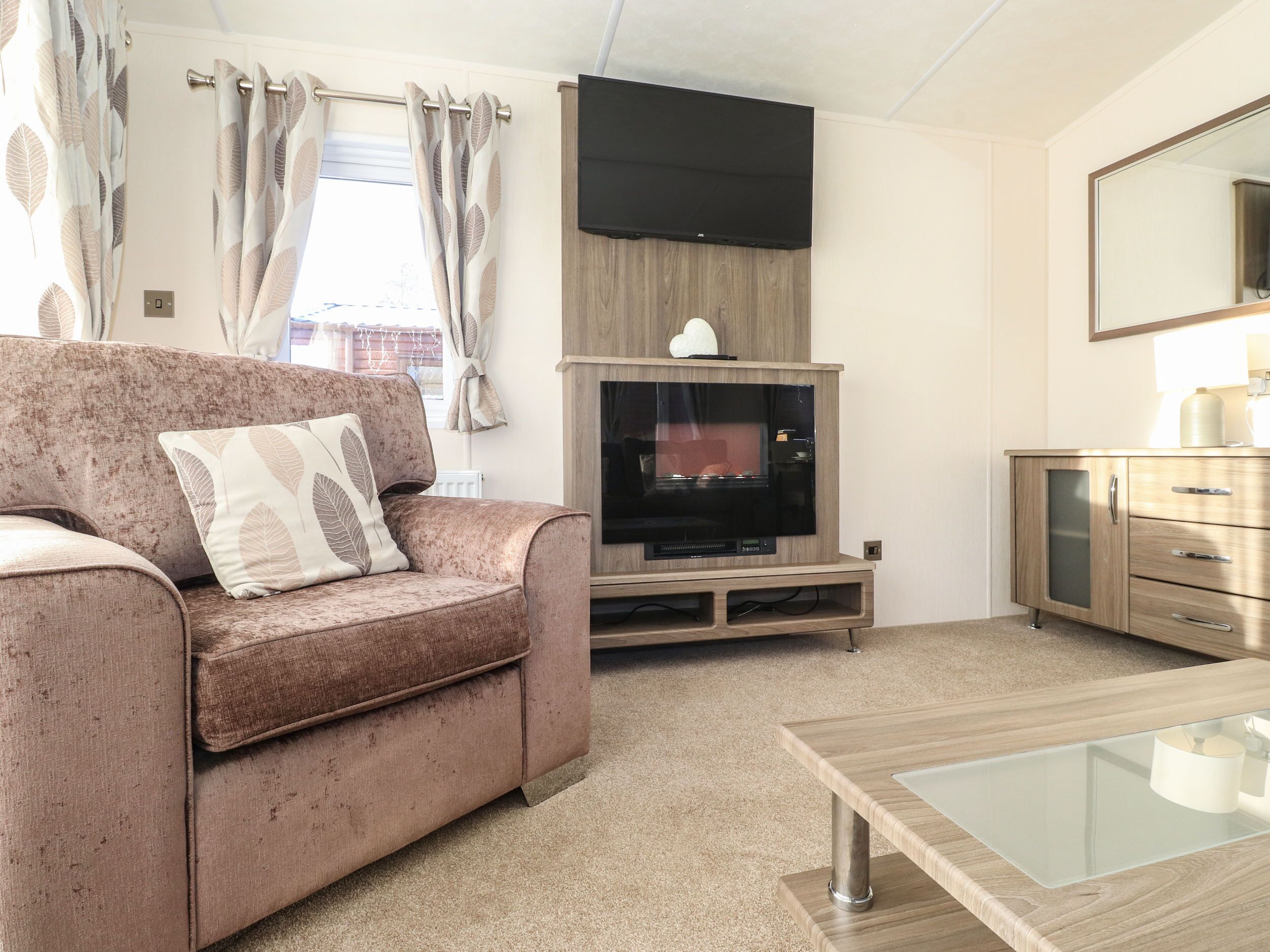 A living room with a sofa, a flat-screen TV, a wooden cabinet, and a glass coffee table.