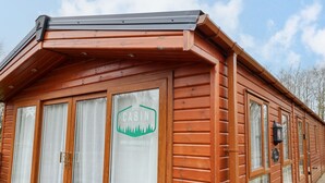 A wooden cabin with large windows, a sign reading "Cabin Escapes," and a website address. - Hercules (Morpeth)
