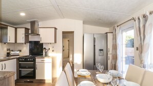 A compact kitchen with modern appliances, a dining area with a table set for four, and a view through a window. - Hercules (Morpeth)