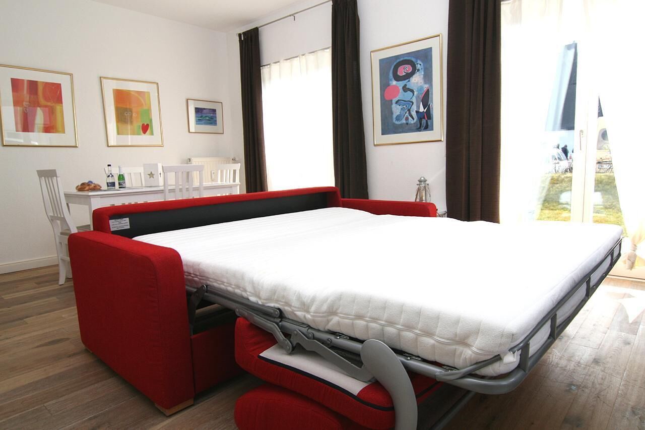 Een kleine kamer met een uitschuifbed, een bureau met stoelen en kunstwerken aan de muur.