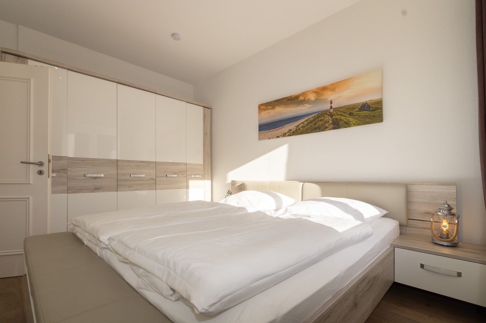 Une chambre à coucher avec un grand lit, une armoire, une table de chevet avec une lanterne et un tableau au mur.
