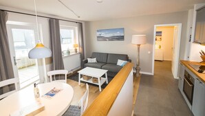 A modern living room with a sofa, a dining table, and a kitchen area. - The Leuchtfeuer apartment is located in the Atair house in Hörnum.... (Hörnum auf Sylt)