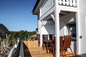 Un ponte di legno con tavolo e sedie, un edificio bianco con un balcone e un cielo azzurro limpido.