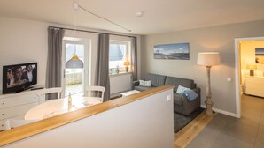 A modern living room with a sofa, a dining table, and a TV. - The Leuchtfeuer apartment is located in the Atair house in Hörnum.... (Hörnum auf Sylt)