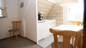 Eine kleine Küche mit Kaffeemaschine, Spüle und gefliestem Rücksprung. Im Raum steht ein Stuhl und ein Tisch.